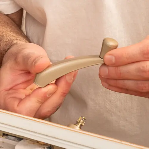 Hands holding a beige casement window crank handle above an operator spline on a window sill.