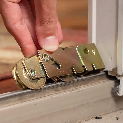 A hand placing a metal tandem roller assembly onto a sliding glass door track.