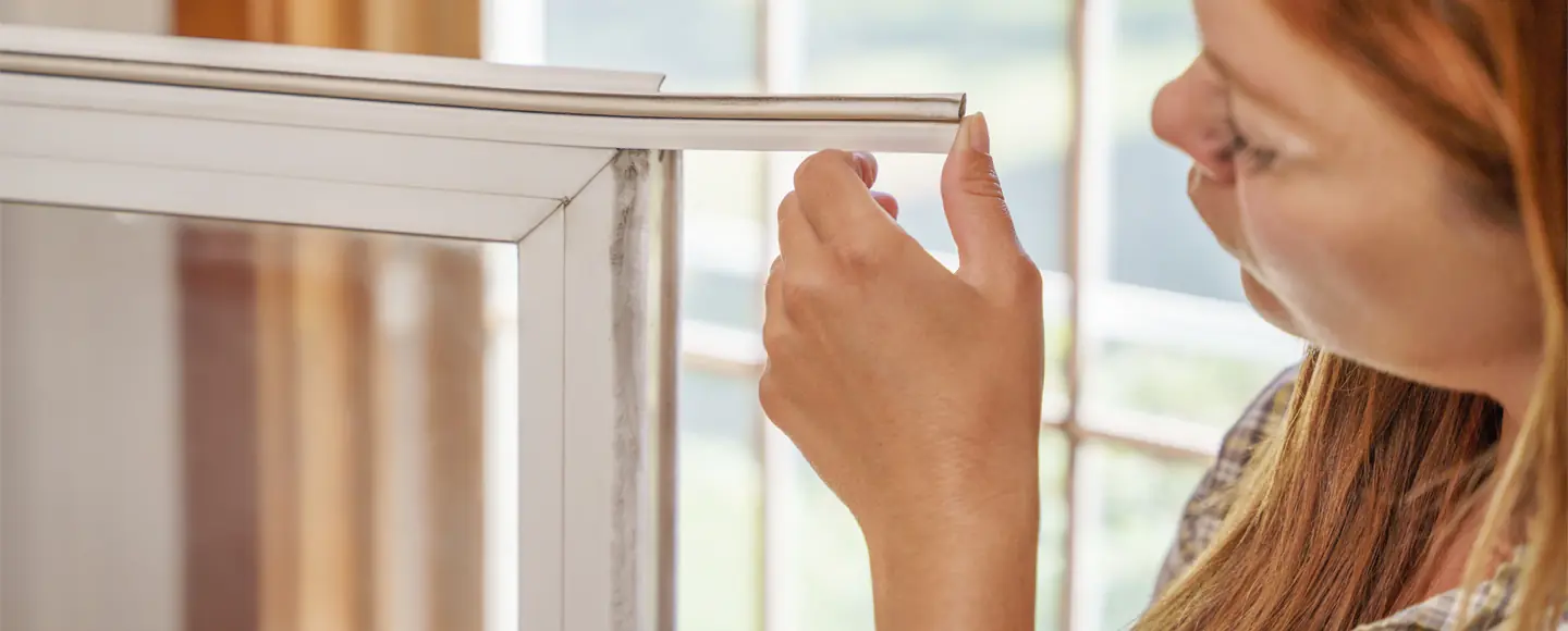 Woman's hand holding and examining the edge of a vinyl window weatherseal during a home draft-proofing repair.