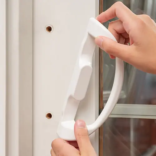 Hands aligning a white sliding patio door handle with the mounting holes on a door frame.